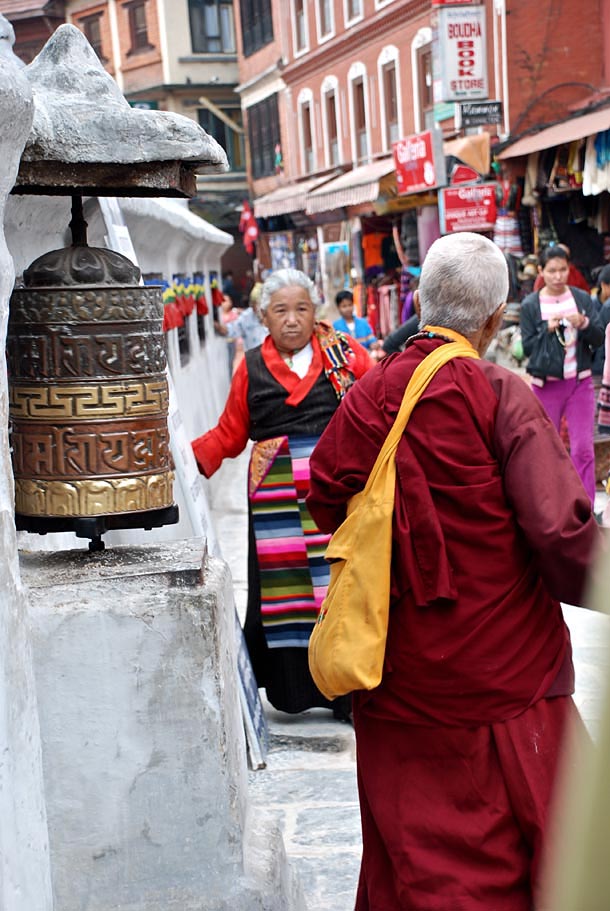 A Buddhist practitioner walks past a line of prayer wheels spinning them while chanting Mantras